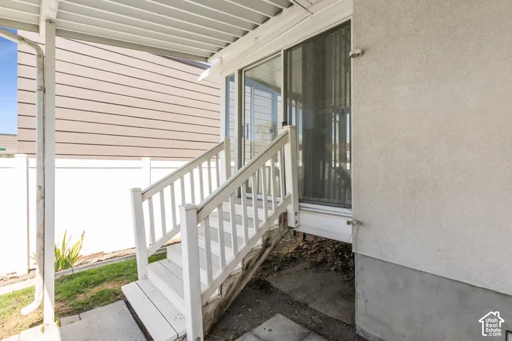 Rear Covered Entry featuring a white aluminum railing, concrete foundation, and direct access to the home via glass sliding doors.  Enters into Enclosed Porch
