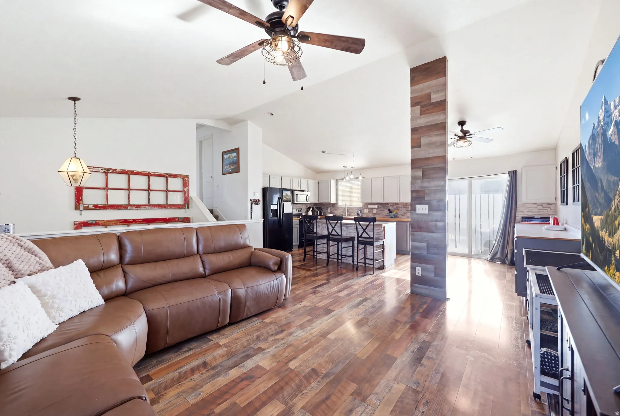 Open-concept living space featuring a brown leather reclining sectional, wood-finish plank flooring throughout, and a ceiling fan with integrated lighting