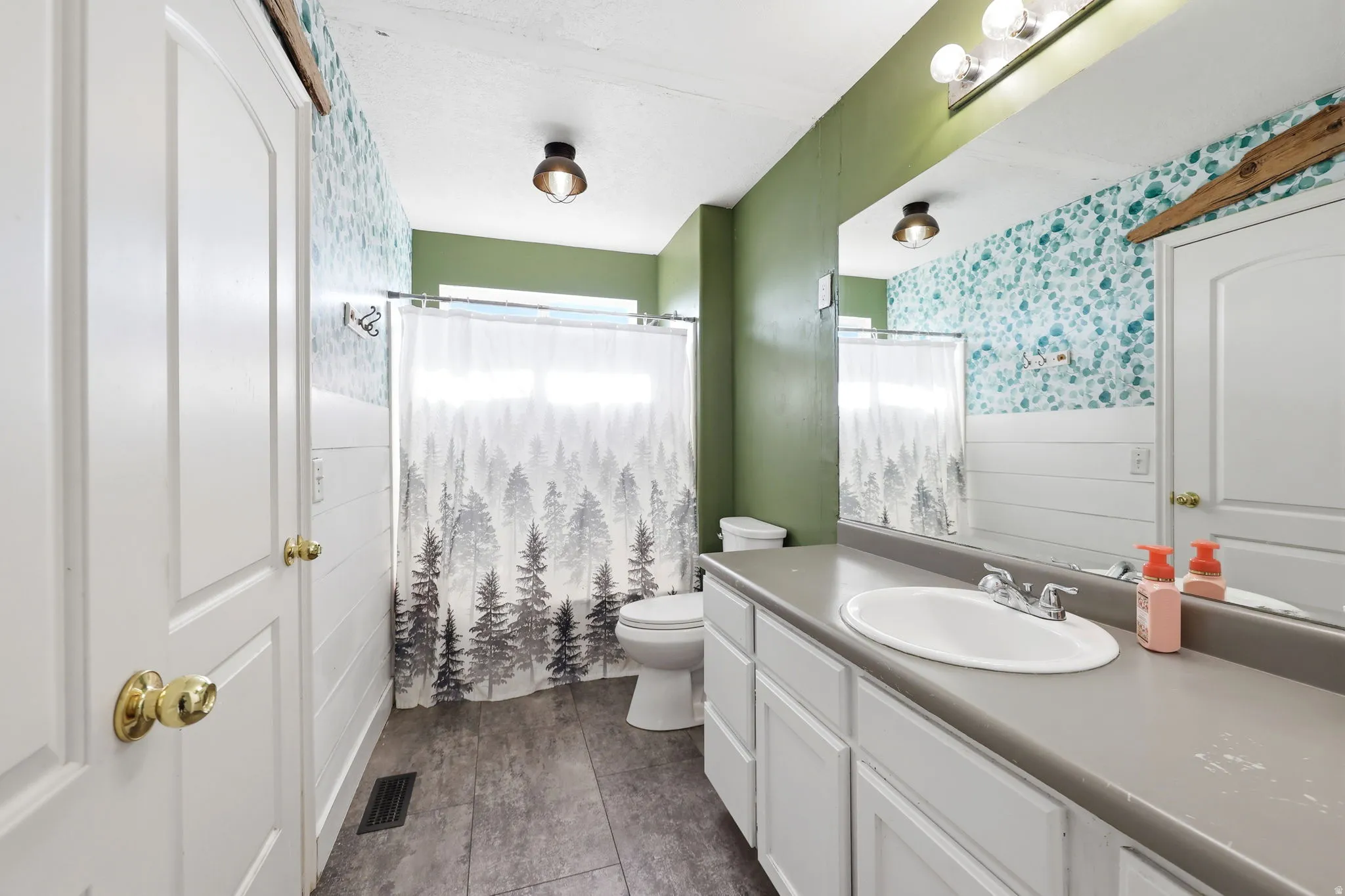 Spa-inspired bathroom featuring soft sage green walls, dual vanity with gray quartz countertop and round vessel sink, polished brass hardware, mosaic tile accent wall, and large mirror with integrated lighting