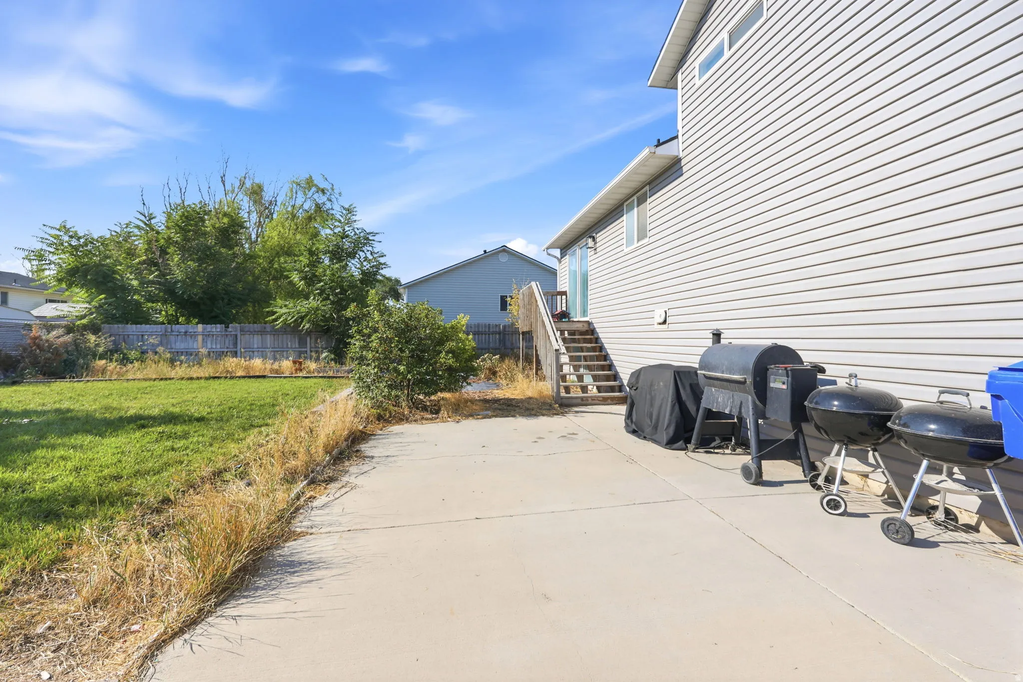 Spacious concrete patio with direct access to the home's rear entrance, complemented by a level lawn with mature landscaping and wooden perimeter fencing