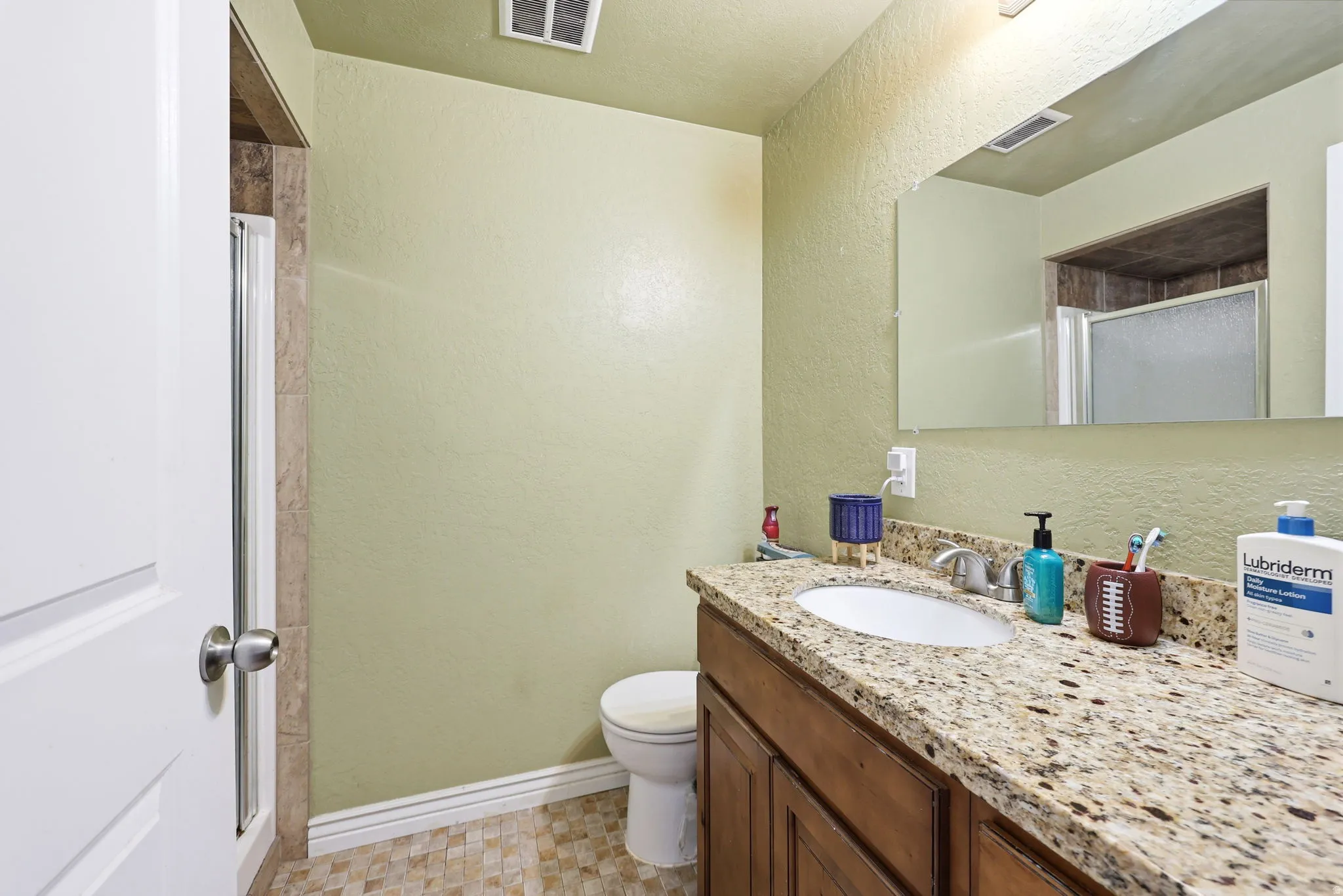 Spacious bathroom featuring a granite-topped dual-sink vanity with wood cabinetry, recessed lighting, and a separate water closet