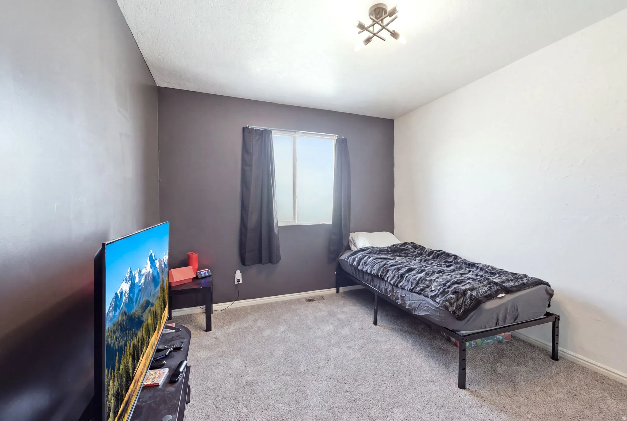 Comfortable bedroom featuring neutral carpet flooring, a single bed frame, recessed ceiling lighting, and a window with dark curtains