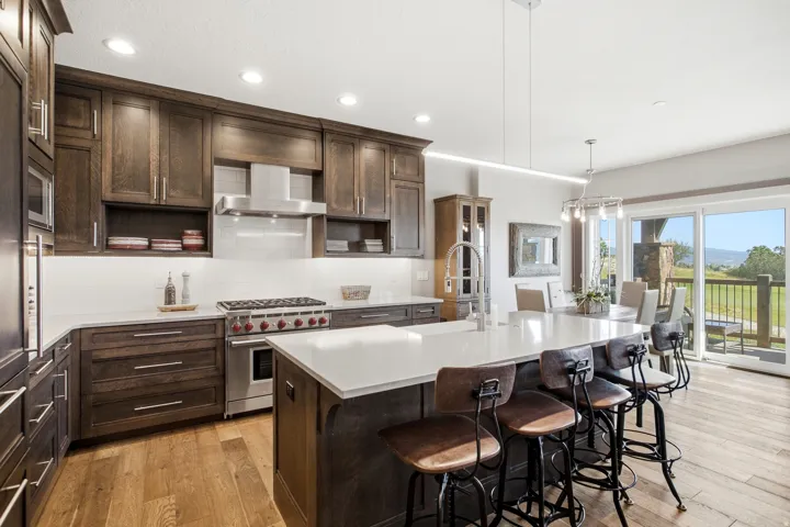 Chef's kitchen featuring custom wood cabinetry, stainless steel appliances including a six-burner range, quartz countertops, and a large waterfall-edge island with seating for multiple guests