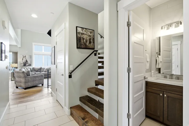 Entryway featuring light-toned rectangular tile flooring, a modern floating staircase with a black handrail, and a powder room with a dark wood-finish vanity and white countertop