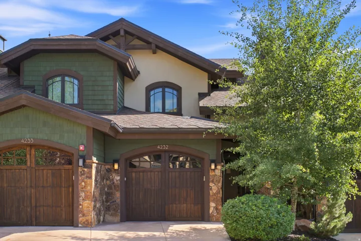 Elegant two-story residence featuring a striking mixed-material exterior with stone accents and wood-finish garage doors