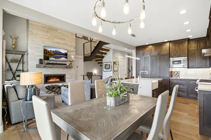 Open-concept living space featuring a wood-finish dining table with herringbone pattern top, paired with upholstered dining chairs