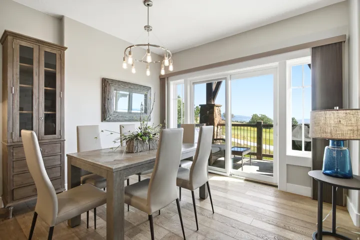 Elegant dining room featuring a wood-finish table with upholstered seating, pendant lighting fixture, and direct access to a covered balcony