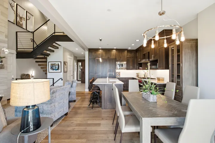 Open-concept living featuring a chef's kitchen with dark wood cabinetry, stainless steel appliances, and a large center island with seating, paired with a dining area and wood-finish flooring throughout