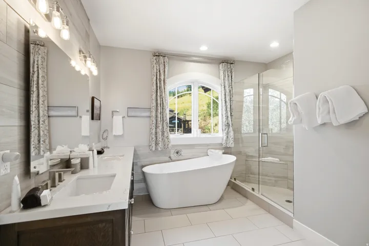 Spa-inspired primary bathroom featuring a freestanding soaking tub, dual-sink vanity with quartz countertop, frameless glass-enclosed shower with tile surround, heated towel rack, and recessed lighting throughout