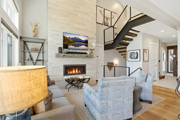 Open-concept living area showcasing a white brick fireplace with integrated gas insert, floating staircase with metal railings, recessed ceiling lighting, and hardwood flooring throughout