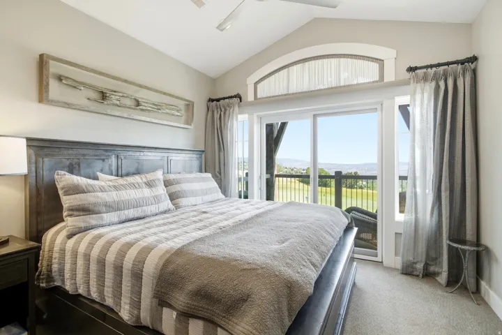 Master bedroom suite featuring a wood-finish platform bed, layered striped bedding, dual nightstands with task lighting, and a vaulted ceiling with ceiling fan