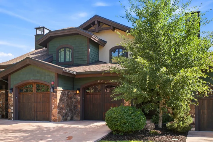 Craftsman-style exterior featuring green shingle siding, natural stone accents, and two wood-paneled garage doors with arched tops