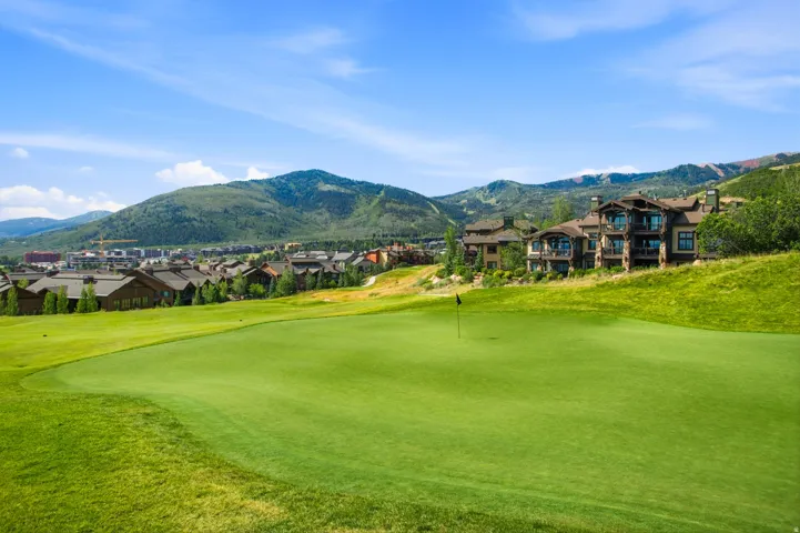 Expansive golf course green with flagstick, bordered by rolling, verdant hills and distant mountains