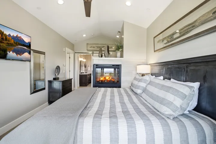 Master bedroom suite featuring a striking black upholstered headboard, striped bedding in neutral tones, and recessed ceiling lighting