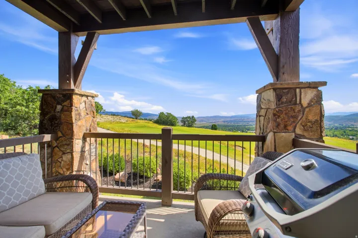 Covered pergola with stone support columns and metal railing overlooking expansive rolling countryside