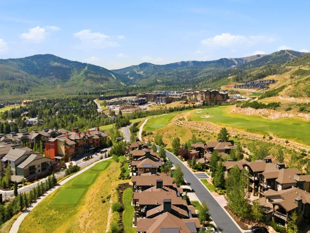 Expansive residential community nestled in a mountain valley setting, featuring multiple brown-toned residential structures with pitched rooflines positioned along tree-lined streets
