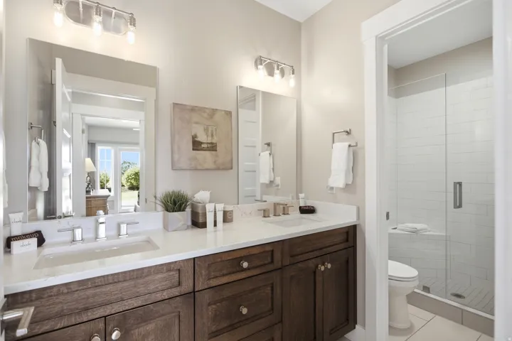 Spa-inspired primary bathroom featuring a dual-sink vanity with rich wood cabinetry, white quartz countertops, and polished nickel hardware