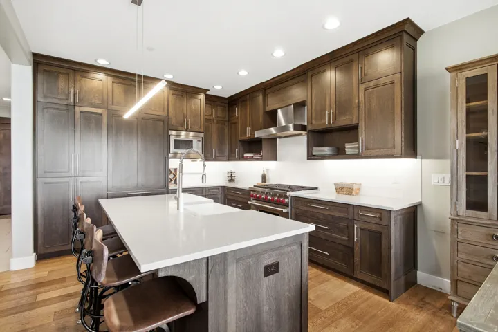 Gourmet kitchen featuring a large central island with integrated sink, wood-finish flooring, dark wood cabinetry, white countertops, and stainless steel appliances