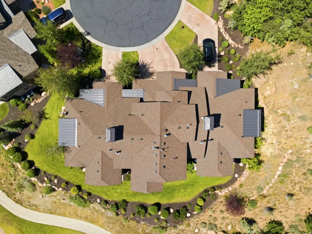 Aerial view showcasing this substantial residential property featuring a multi-level architectural design with a complex roofline, dimensional asphalt shingle roofing, and multiple roof planes
