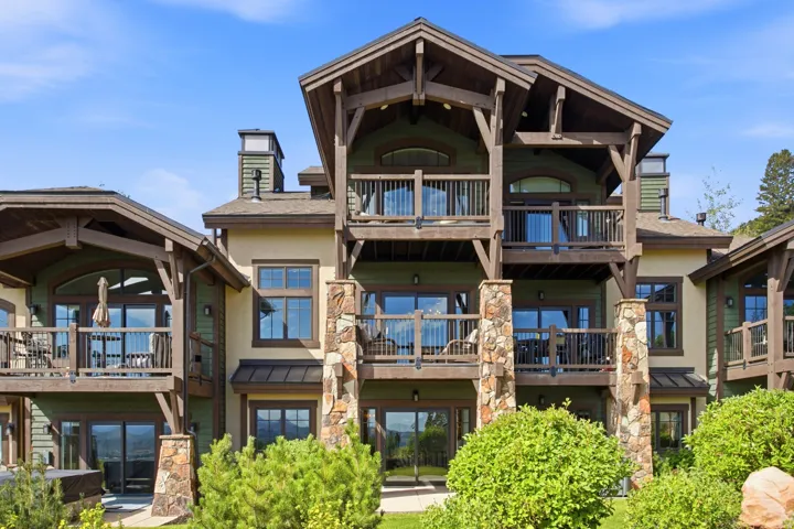 Architectural masterpiece featuring a striking multi-story stone and timber exterior with expansive glass panels, multiple tiered decks with metal railings, and dramatic pitched rooflines with exposed beam detailing