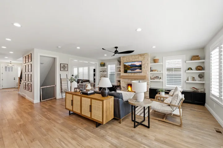 Spacious living area featuring a stacked stone fireplace with a wood mantle, custom built-in shelving, wood-finish flooring, recessed lighting, and white plantation shutters