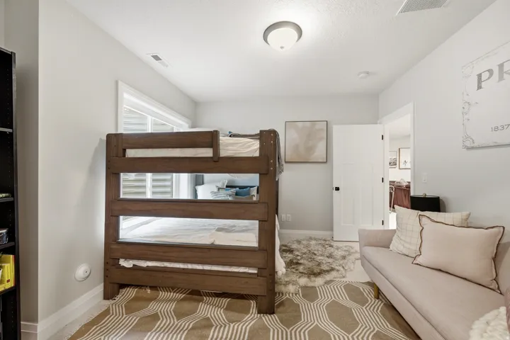 Spacious bedroom featuring a sturdy wood bunk bed with multiple sleeping tiers, geometric patterned area rug, recessed ceiling lighting, and abundant natural light from transom windows