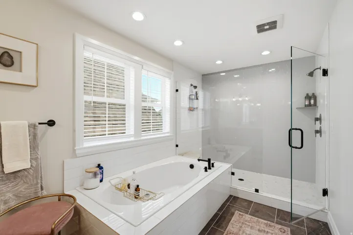 Contemporary bathroom featuring a built-in soaking tub with matte black fixtures, a spacious walk-in shower with glass enclosure, white subway tile accents, recessed lighting, and dual windows with blinds