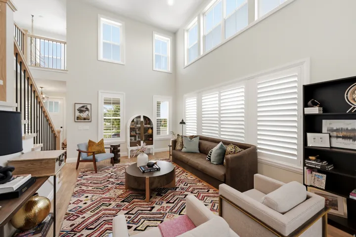 Soaring two-story living room featuring floor-to-ceiling windows, white plantation shutters, and abundant natural light