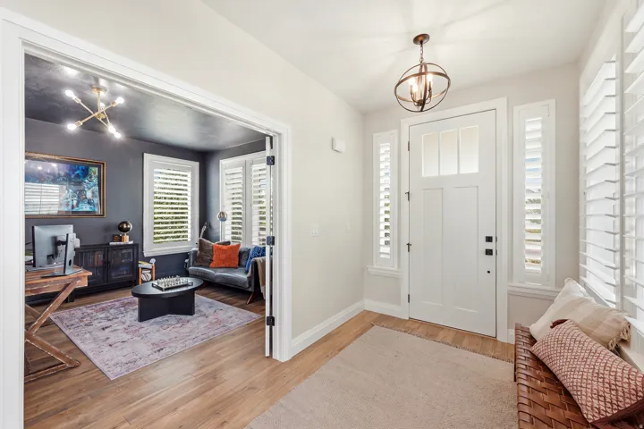 Welcoming foyer showcasing wood-finish flooring, white six-panel doors with sidelights, and a pendant light fixture