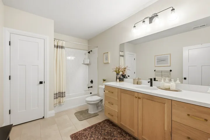 Bathroom featuring a dual-sink vanity with light wood cabinetry, white countertops, and contemporary black fixtures