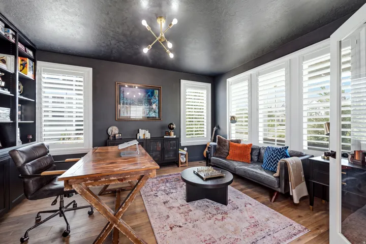 Dedicated space featuring built-in shelving, multiple windows with white plantation shutters, wood-finish flooring, a contemporary chandelier, and French doors