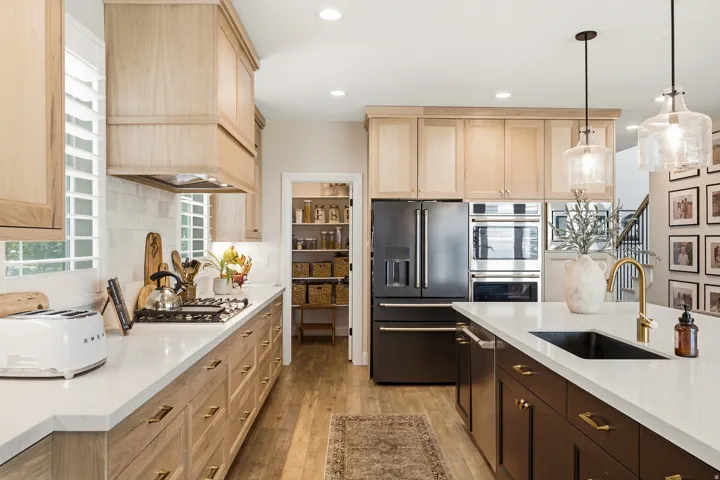 Galley-style kitchen featuring light wood cabinetry, white quartz countertops, and stainless steel appliances including a French-door refrigerator and built-in wall oven