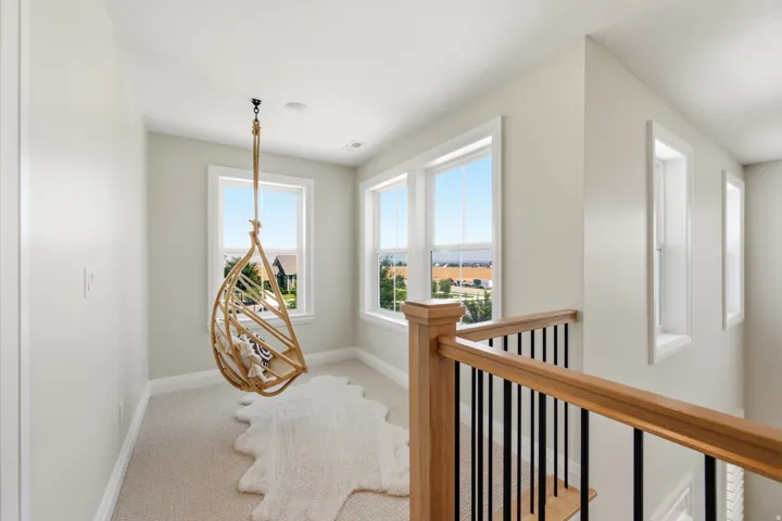 Carpeted landing featuring multiple windows, a natural wood handrail with black metal balusters, and light-toned wall finishes