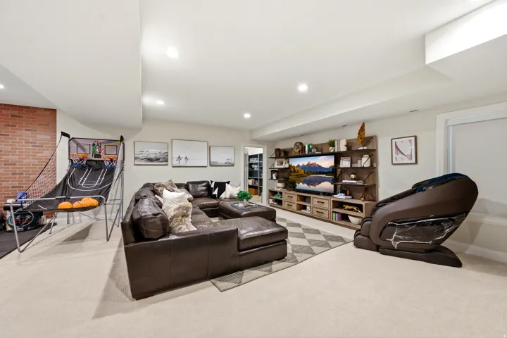 Spacious room featuring light-toned carpet flooring, recessed lighting, and a prominent media wall unit with open shelving and closed storage