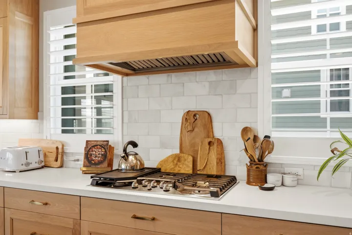 Gourmet kitchen featuring a stainless steel gas range, light wood-finish cabinetry, a white subway tile backsplash, and light-toned countertops
