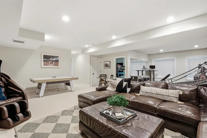 Expansive recreation room featuring recessed ceiling lighting, engineered wood-finish flooring, and a geometric area rug