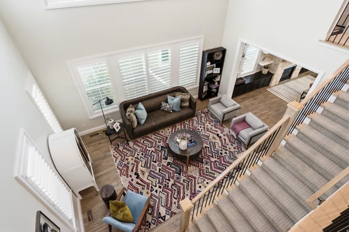 Two-story living area with high ceilings, wood-finish flooring, and white plantation shutters