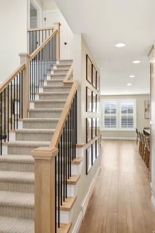 Elegant foyer and staircase featuring wide plank wood-finish flooring, a custom wooden handrail with black metal balusters, and recessed ceiling lighting