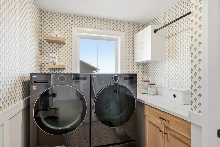 Dedicated laundry space featuring patterned wallpaper, a white window frame, and two wood-finish floating shelves