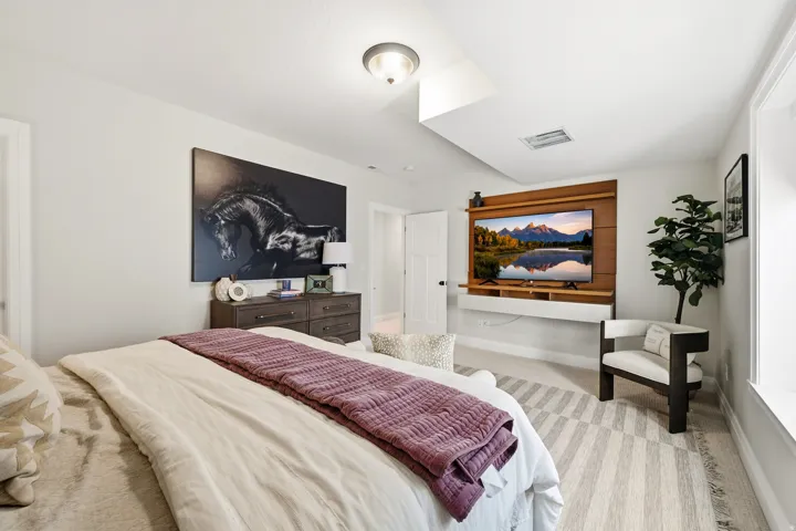 Bedroom featuring light-colored walls and a wall-mounted television on a wood-paneled accent wall with a floating shelf