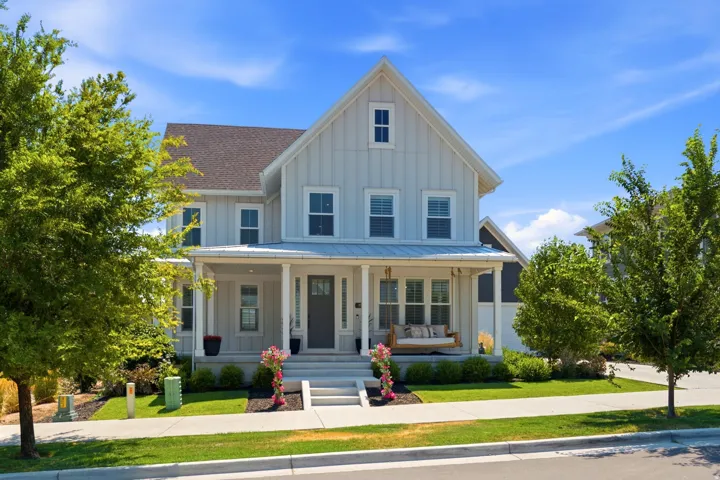 Charming farmhouse-style residence featuring a light blue and white exterior with vertical board-and-batten siding, peaked gable roof with architectural shingles, and a full-width front porch with white columns and railings