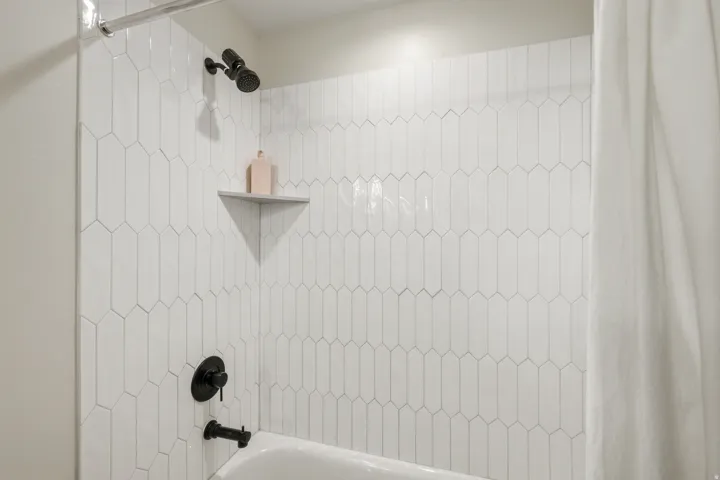 Shower with picket tile surround, matte black fixtures, and a built-in corner shelf