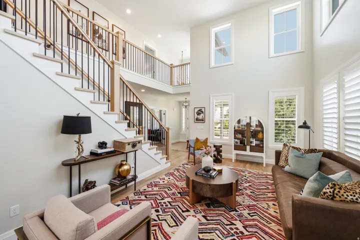 Two-story living area with high ceilings, featuring a grand staircase with wood-finish handrails and black metal balusters