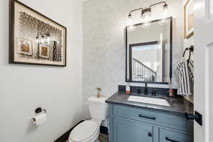 Powder room featuring a subway tile accent wall, a vanity with a dark countertop and integrated sink, a rectangular framed mirror, and a three-light vanity fixture