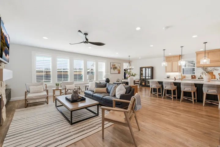 Open-concept living space featuring hardwood flooring throughout, a ceiling fan with recessed lighting, and large multi-pane shuttered windows providing natural light