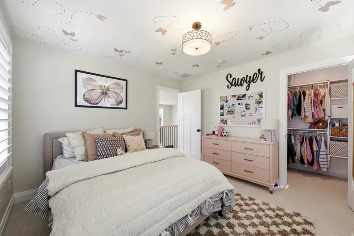 Bedroom featuring light beige wall paint, a built-in closet with shelving and hanging rods, a ceiling light fixture with a decorative metal frame, and a window with white louvered shutters