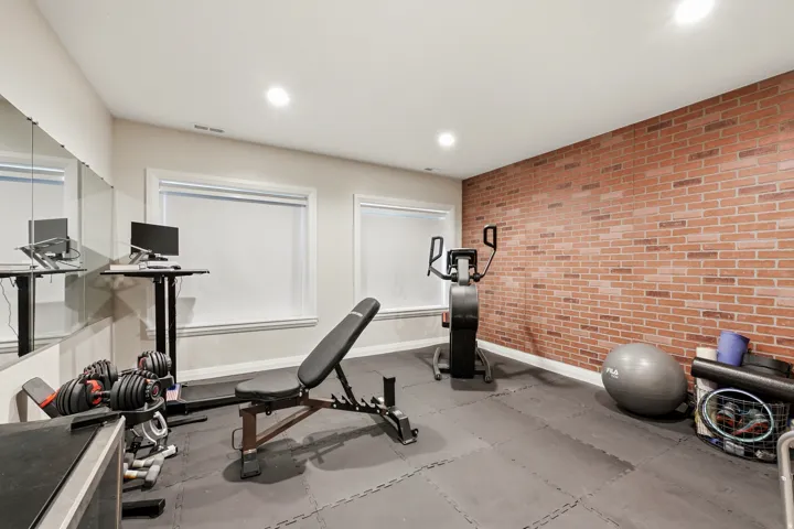 Dedicated fitness space featuring a full brick accent wall, recessed lighting, and resilient interlocking floor tiles