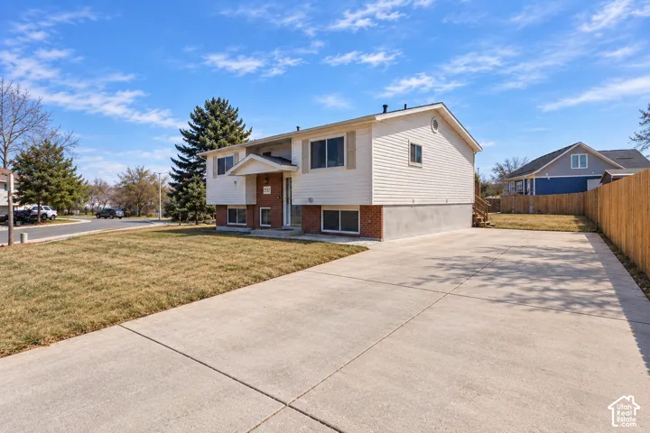 Split-level exterior featuring light-toned horizontal siding, a partial brick facade, an expansive concrete driveway, and a wood privacy fence