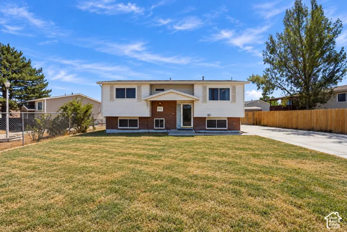 Split-level exterior featuring a brick and siding facade, covered entryway, expansive front lawn, concrete driveway, and wood fencing