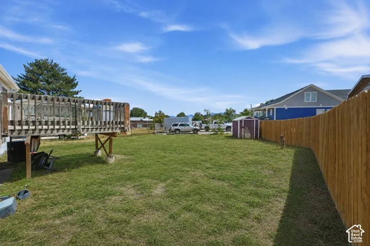 Backyard featuring an elevated wood deck, expansive lawn, perimeter wood fencing, and a detached storage structure